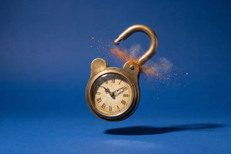 An old brass padlock with a clock face instead of a combination dial floats against a cobalt-blue backdrop, its shackle just snapping open as dust and rust burst from the hinge