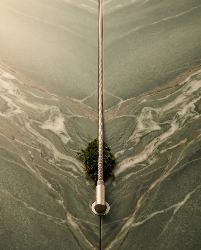 Two book-matched slabs of green Verde marble whose light veins meet at the center joint; a braided cable with a cushion of moss lies in the joint and ends at the bottom in a champagne plug in a socket