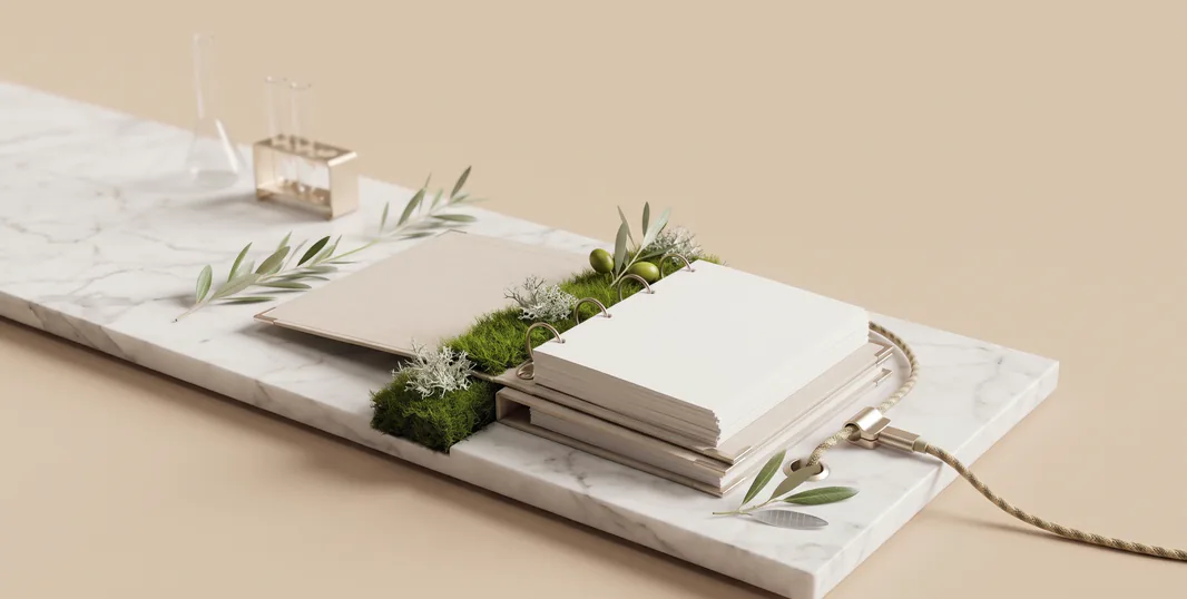 Open documentation binder in sand-colored linen with a champagne-metal ring mechanism on a long Calacatta slab; along the spine, a strip of moss with lichen and an olive branch with green olives grow along a braided cable, and a flask and test tubes stand behind it